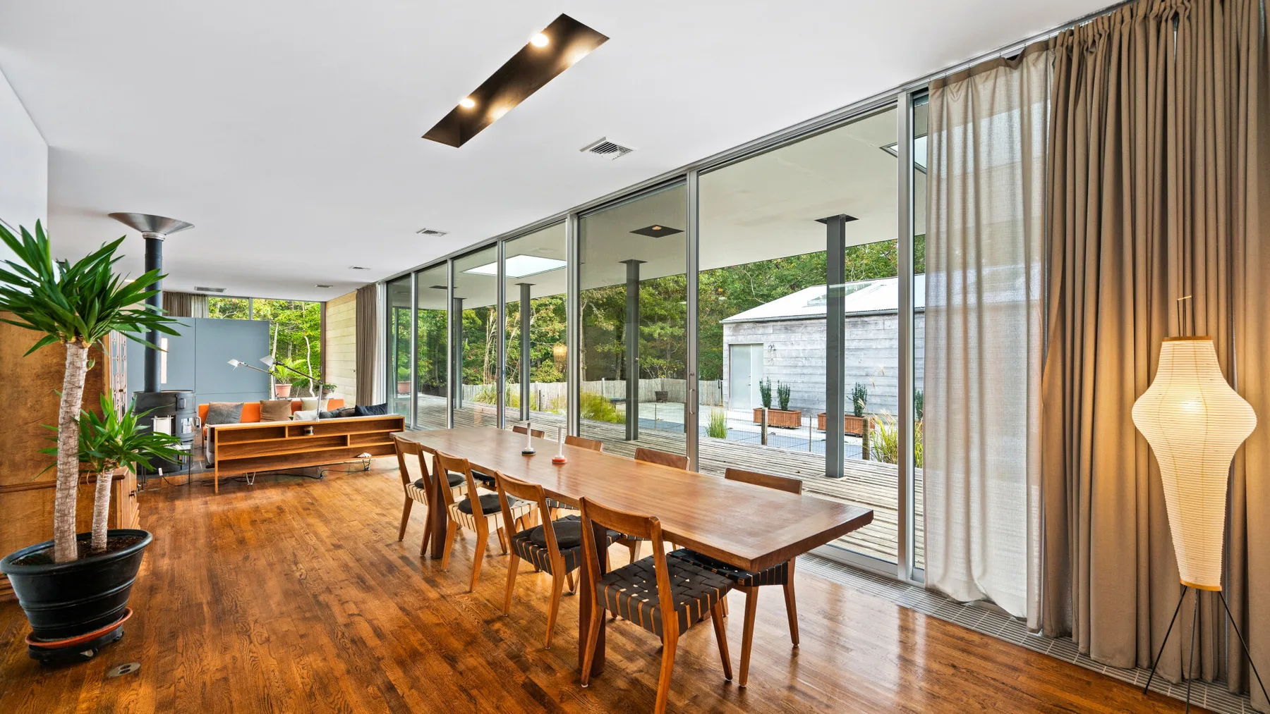 A spacious dining area with a long wooden table beside floor-to-ceiling glass doors.