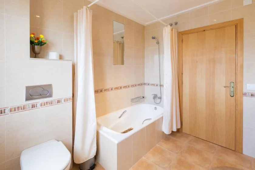 A tiled bathroom with a bathtub, shower curtain, and wooden door.