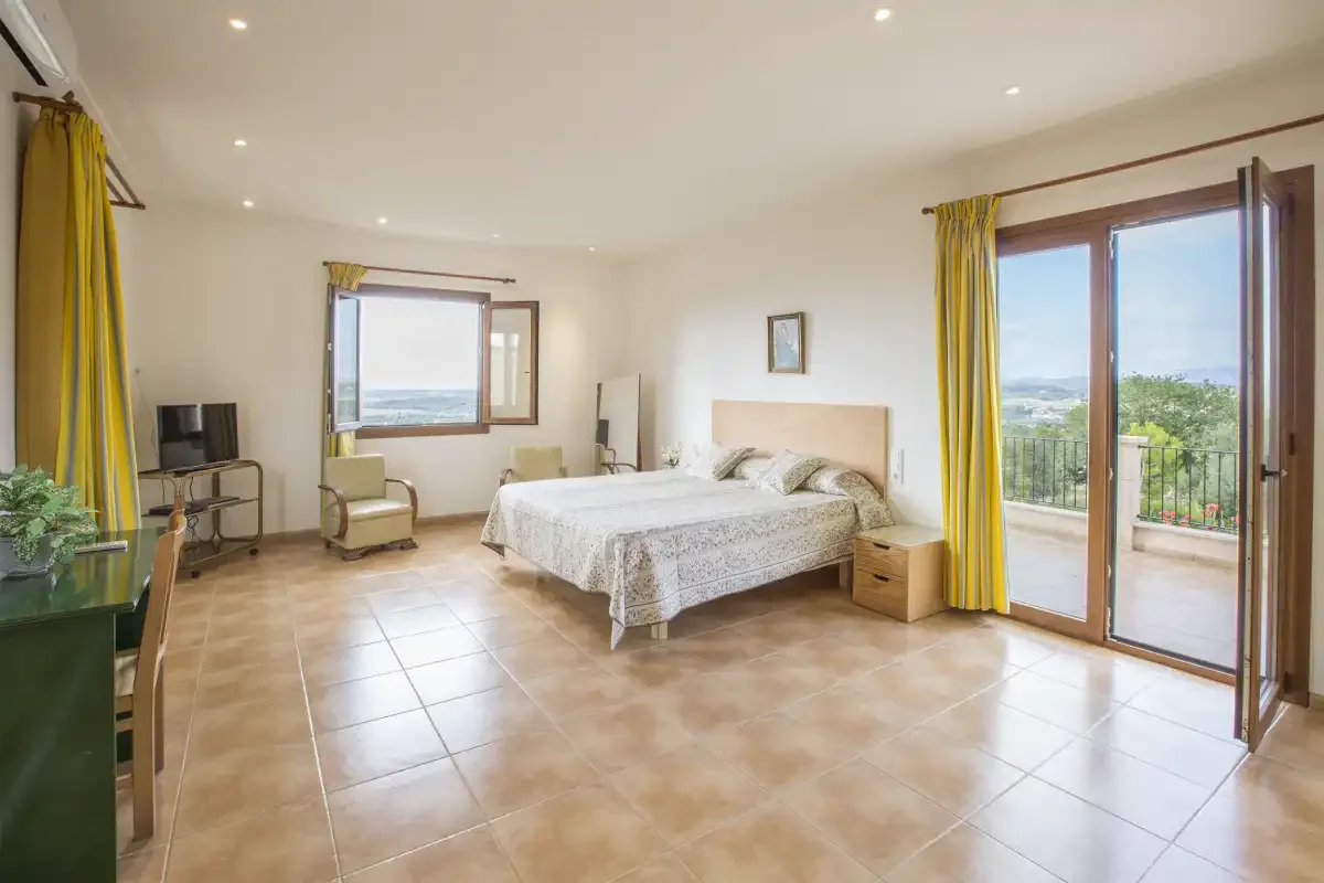 A bright bedroom with a bed, seating, and glass doors opening onto a balcony.