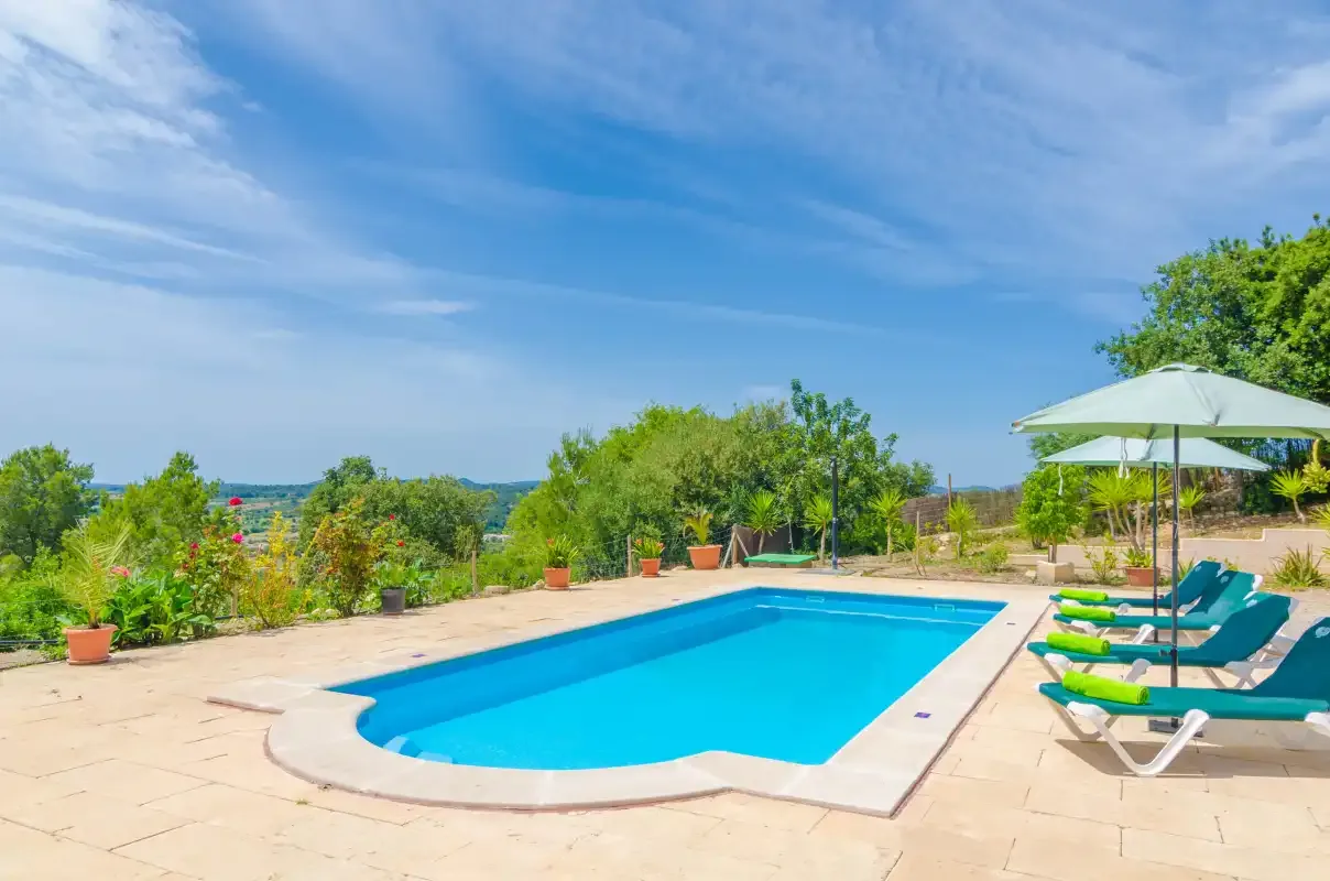 An outdoor swimming pool sits beside lounge seating and an open umbrella.