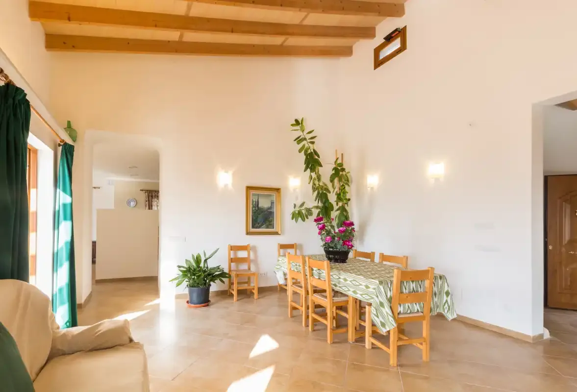A bright dining area with a wooden table and chairs beneath exposed ceiling beams.