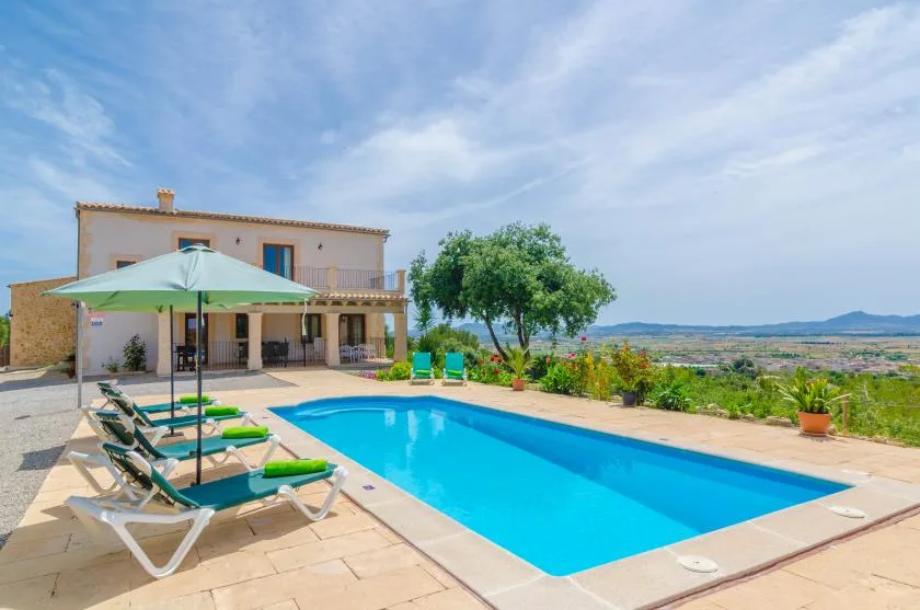 A swimming pool beside a two-story house, with lounge seating on the patio.