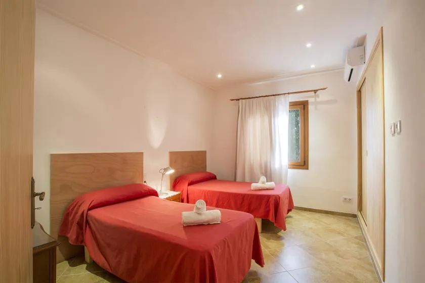 A bedroom with two beds covered in red bedding and a curtained window.