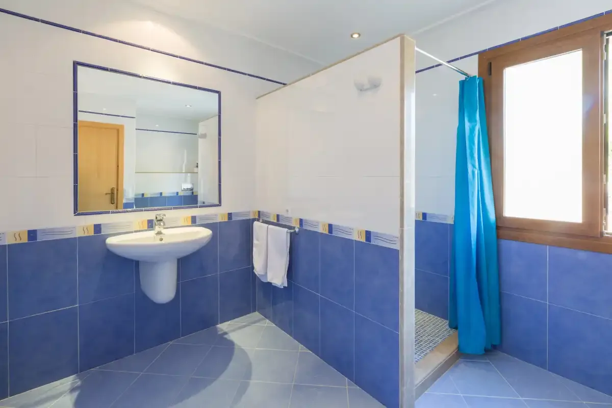 A tiled bathroom has a sink, mirror, and shower with a blue curtain.