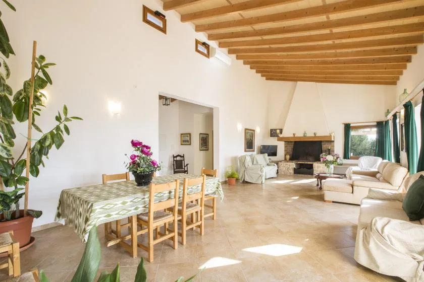 A spacious living and dining room with a wooden-beam ceiling and seating around a fireplace.