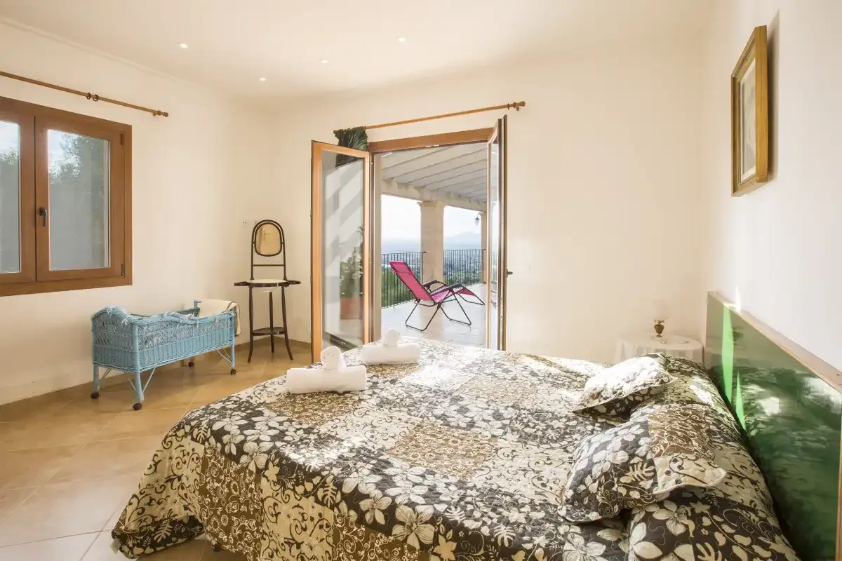 A bedroom with a patterned bedspread and open doors leading to a patio.