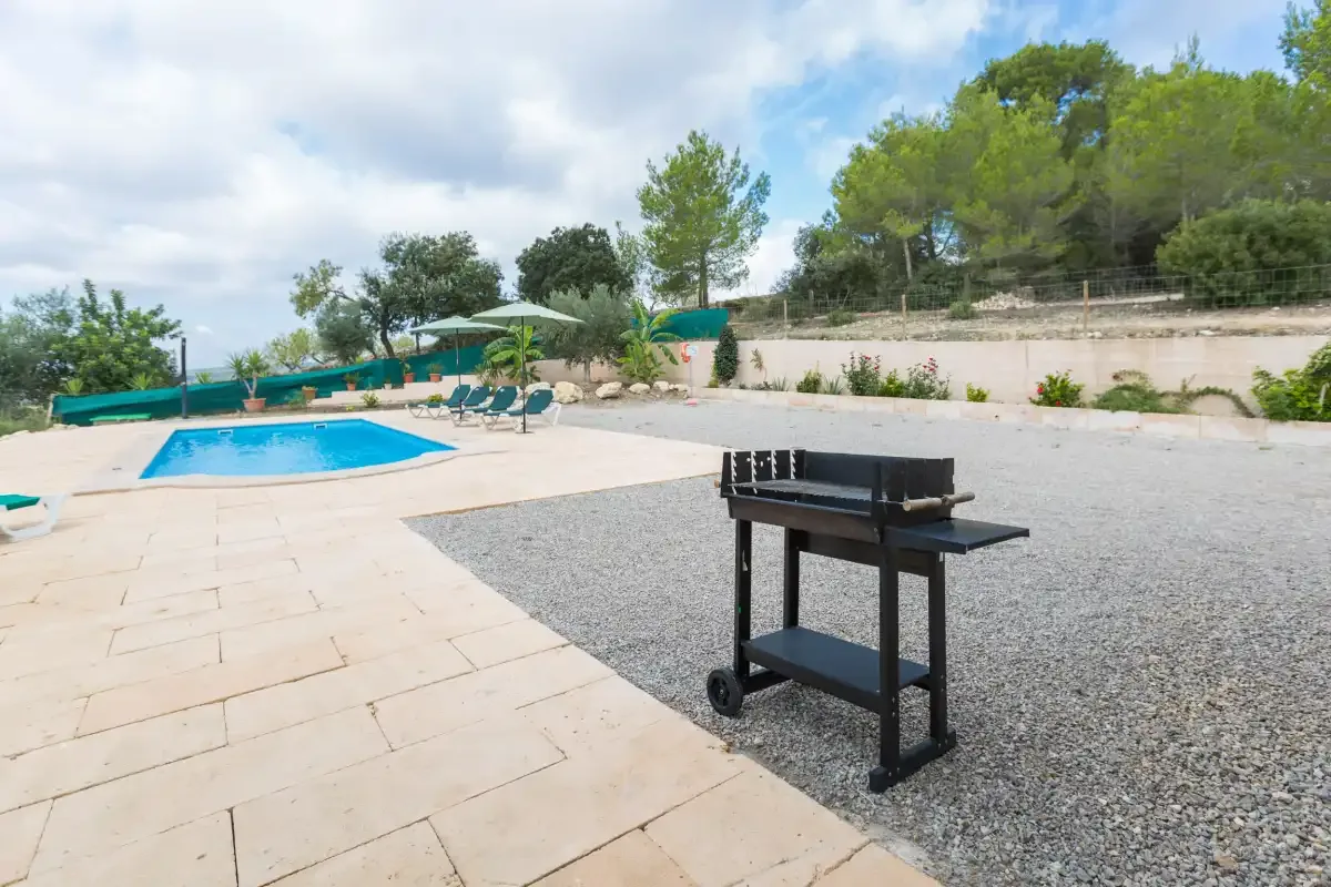 An outdoor pool area with a paved patio and a grill beside the pool.