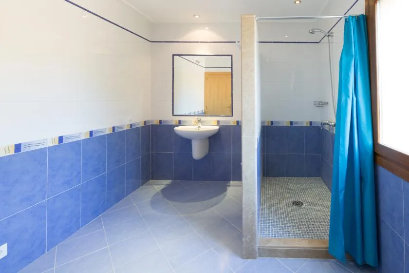 A bathroom with blue tiled walls, a wall-mounted sink, and a curtained shower.