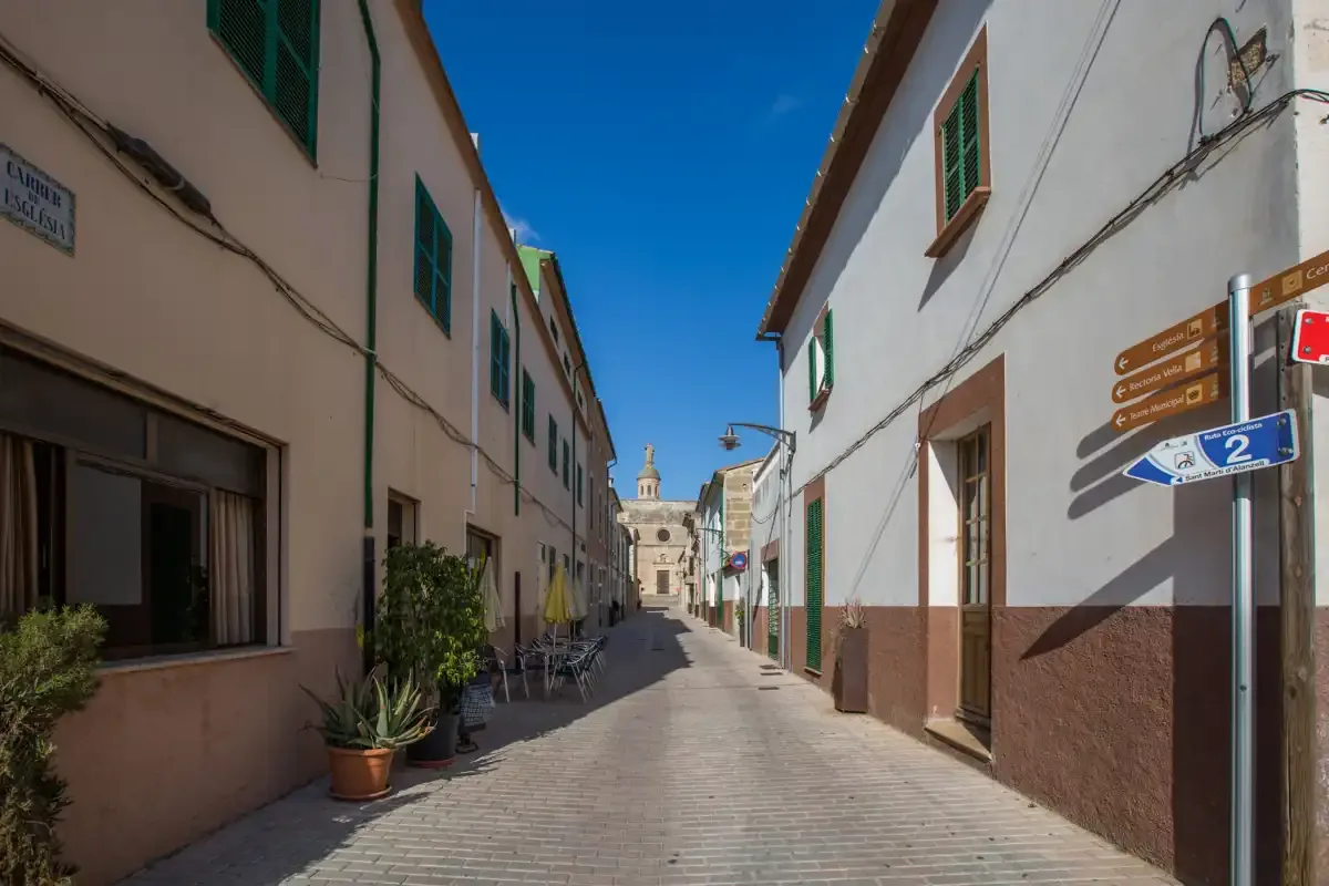 A narrow paved street runs between low-rise buildings beneath a clear blue sky.