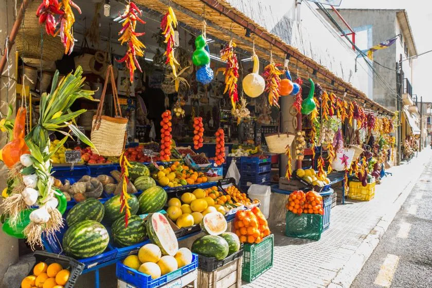 An outdoor market stall displays colorful produce, including watermelons and citrus.