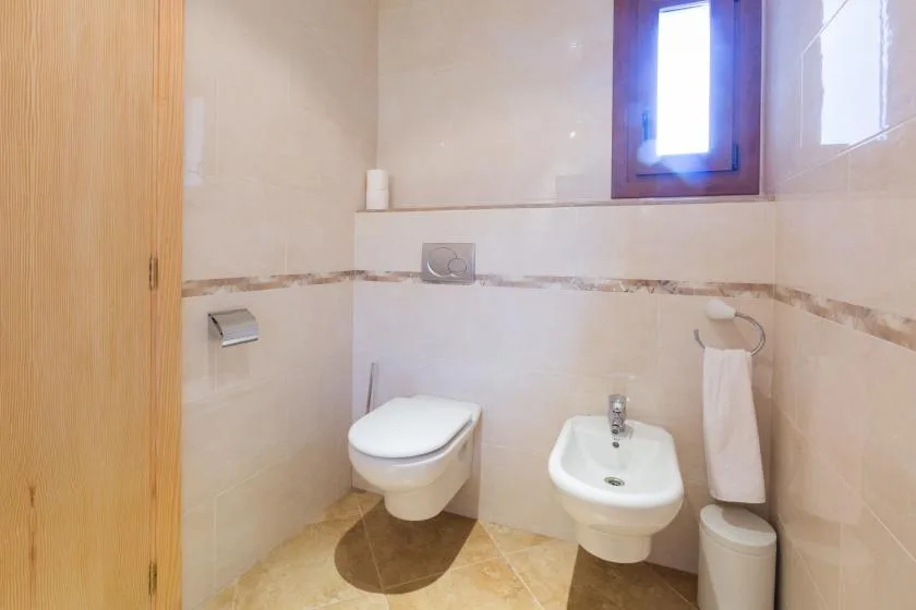 A tiled bathroom with a toilet, bidet, and small window.