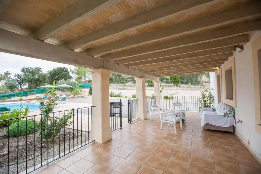 A covered tiled patio overlooks a swimming pool, with outdoor seating nearby.