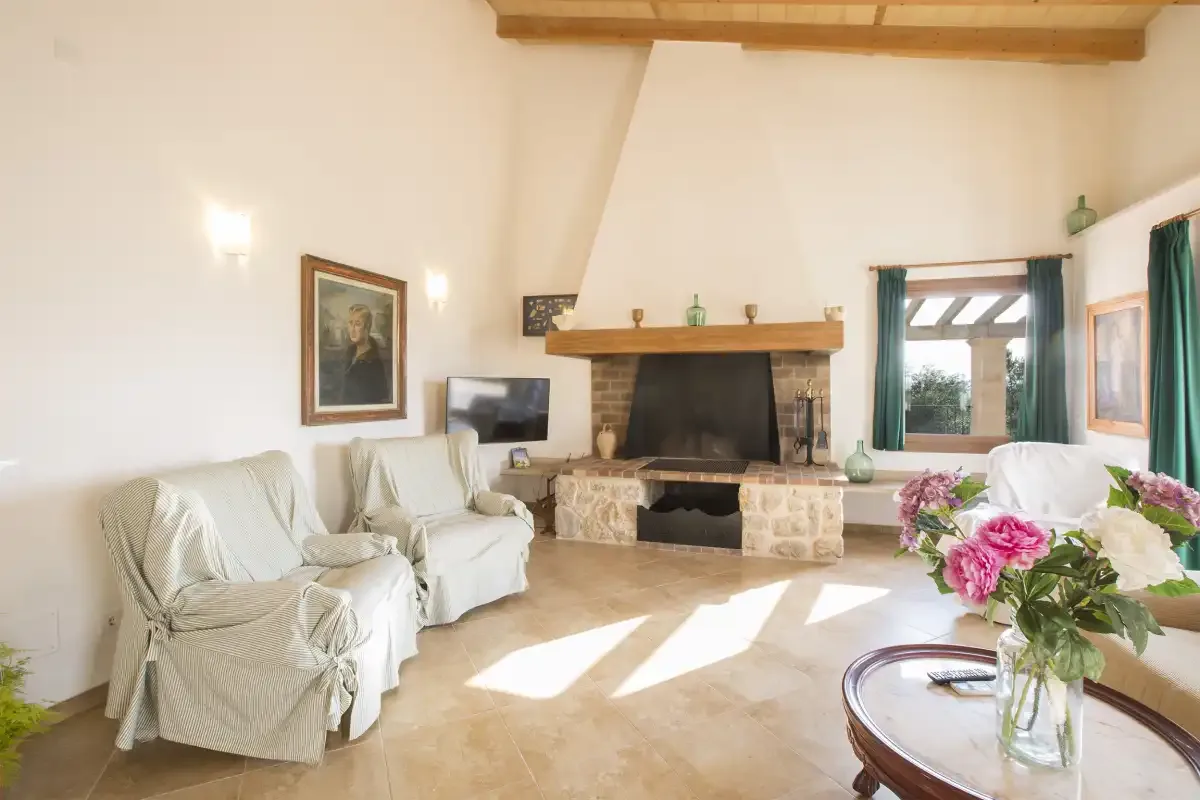 A bright living room has seating around a large fireplace.
