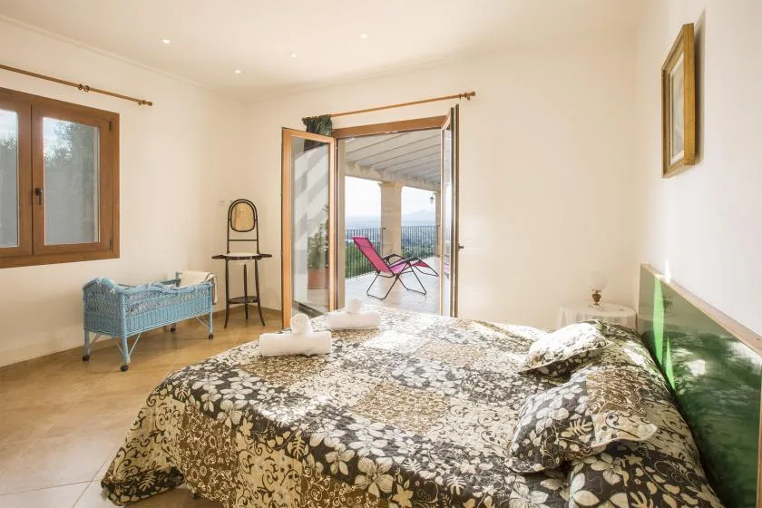 A bedroom with a patterned bedspread and open doors leading to a patio.