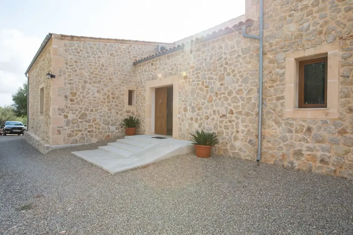 A stone building exterior with a wooden entrance door and gravel forecourt.