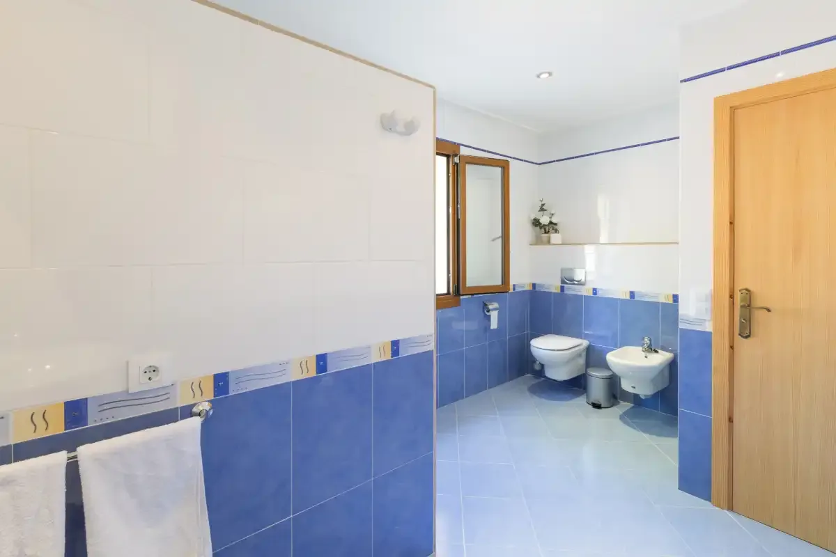 A tiled bathroom with a toilet, bidet, sink, and window.