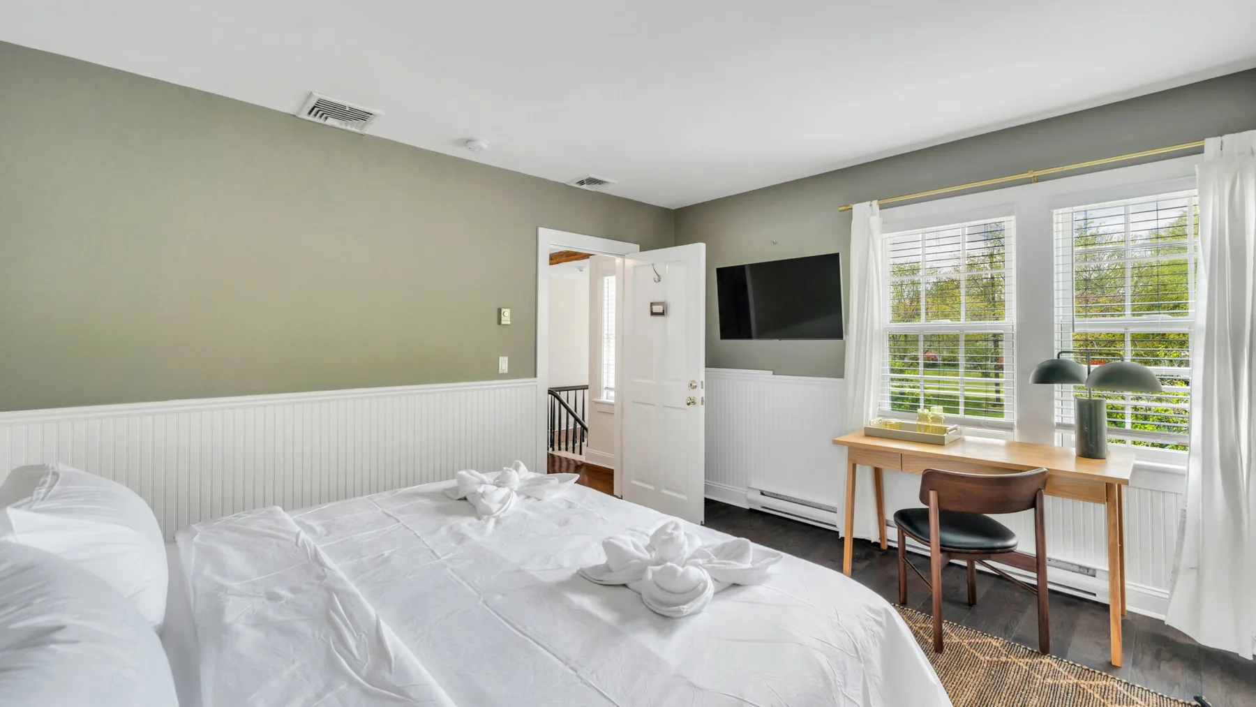 Un dormitorio luminoso con ropa de cama blanca y un escritorio junto a las ventanas.