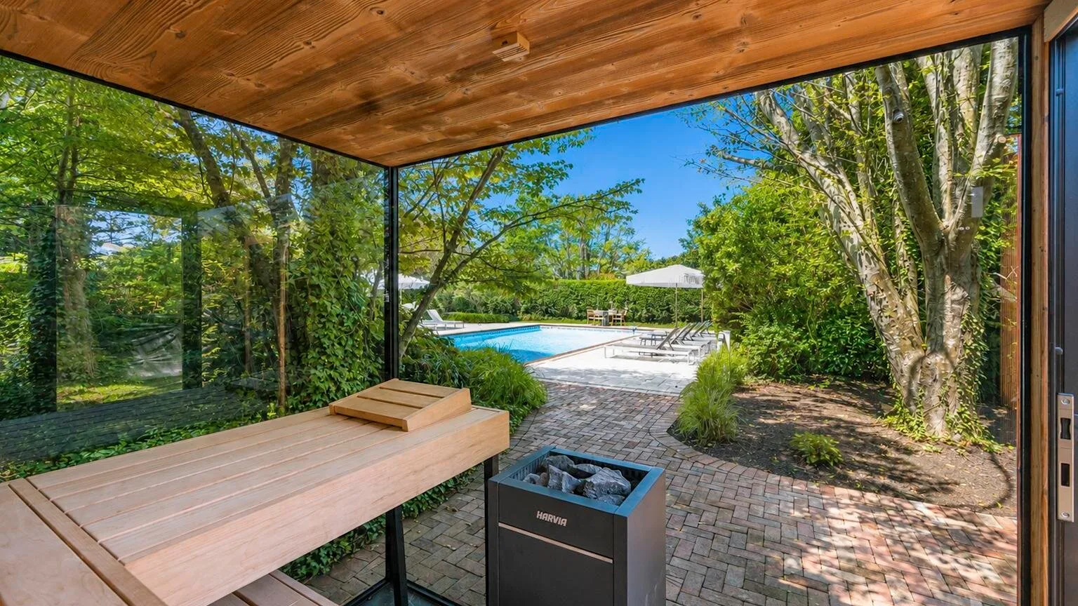 Un patio cubierto da a un jardín, con una piscina visible al fondo.