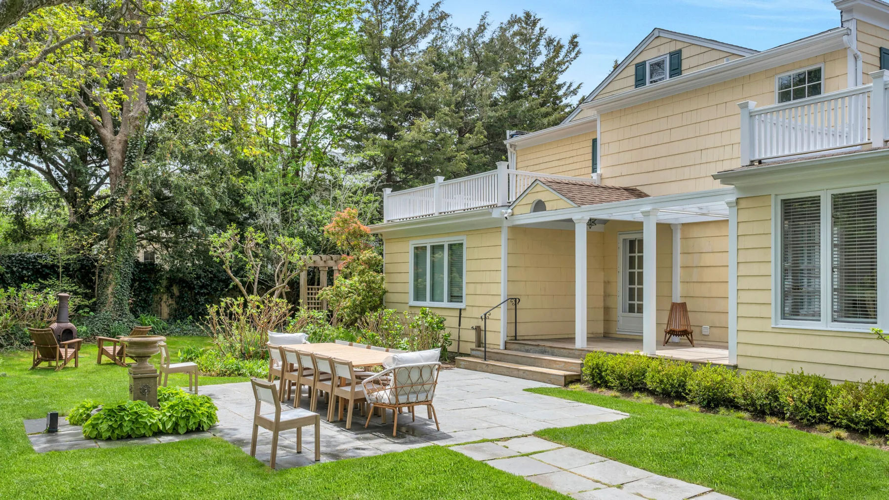 Una casa amarilla da a un patio con muebles de comedor al aire libre y césped verde.