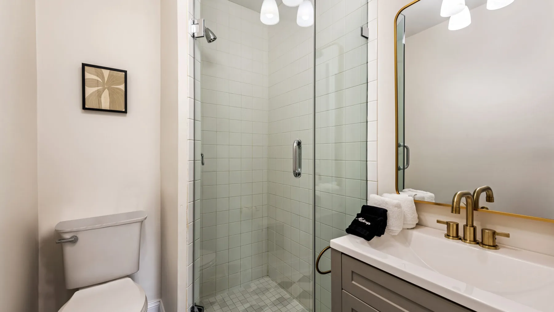 Un baño con una ducha de vidrio y un tocador junto al inodoro.