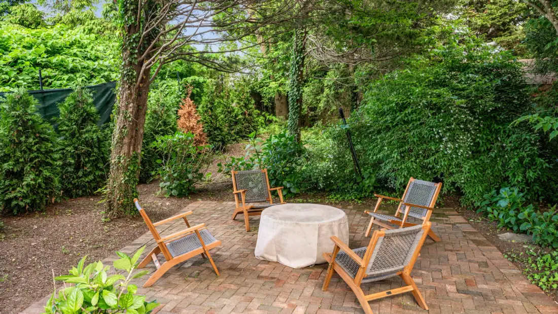 Un patio de jardín con asientos de madera alrededor de una mesa cubierta.