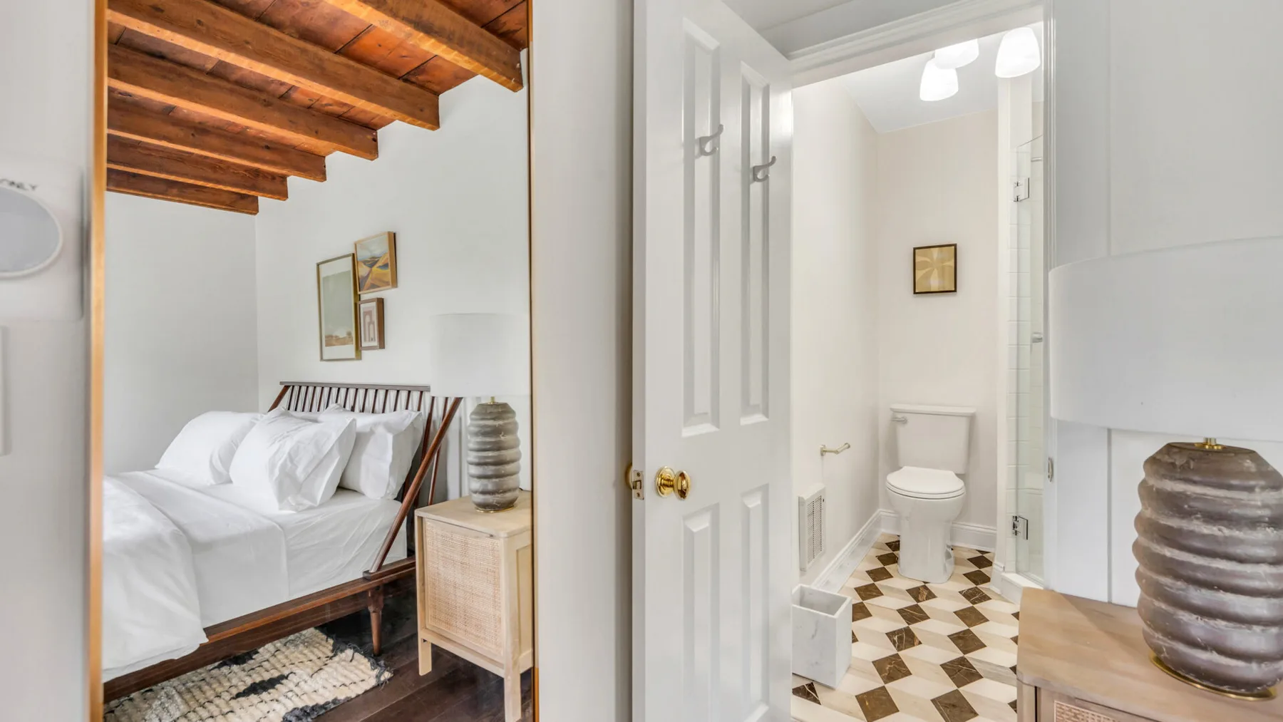Un dormitorio con una cama blanca junto a una puerta abierta hacia un baño.