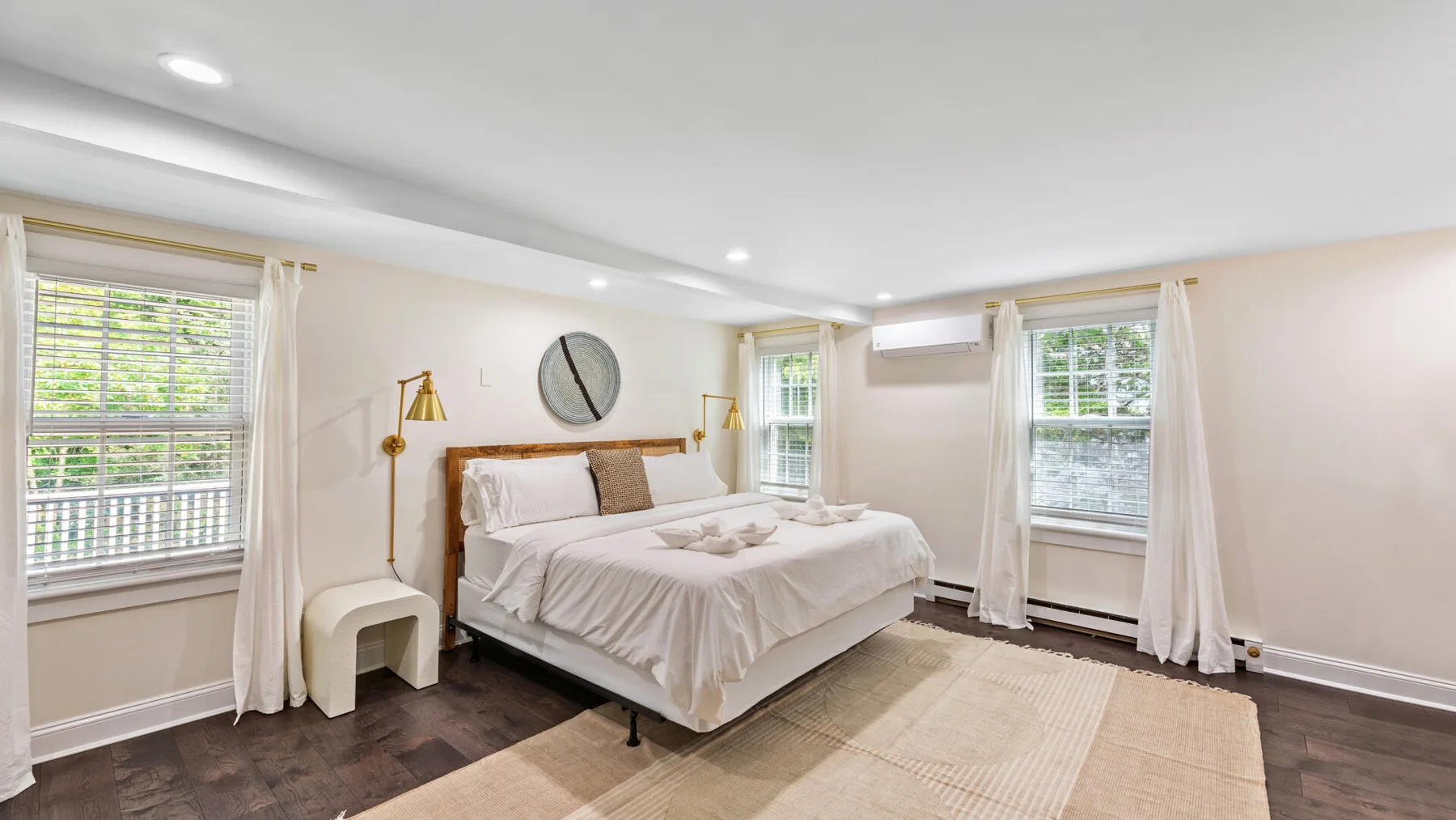 Un dormitorio luminoso con una cama, cortinas claras y varias ventanas.