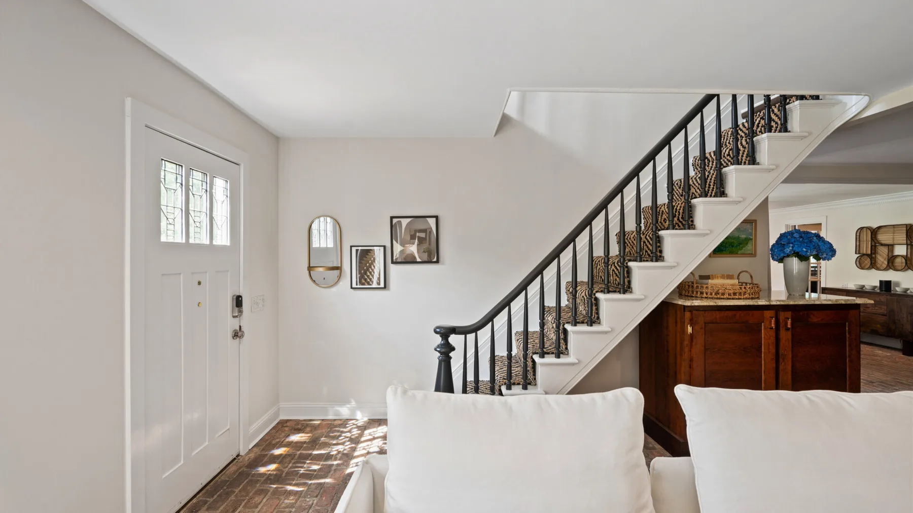 Una sala luminosa con asientos blancos junto a una escalera y una puerta de entrada.