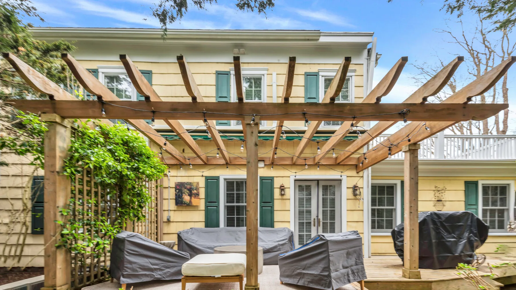 Un patio al aire libre bajo una pérgola de madera, con asientos cubiertos.
