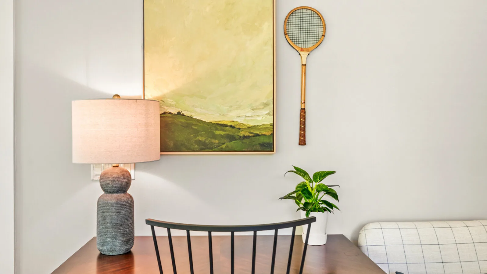 Una zona de descanso en un dormitorio con banco de madera, lámpara de mesa y arte en la pared.
