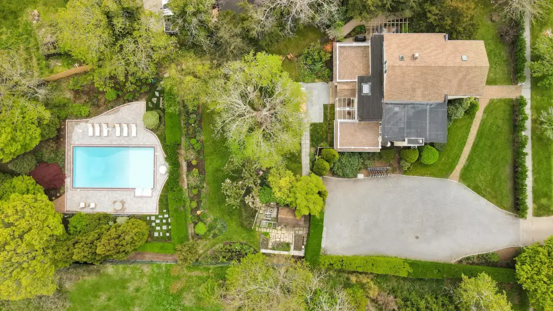 Una vista aérea muestra una casa, una piscina, una entrada para vehículos y un jardín ajardinado.