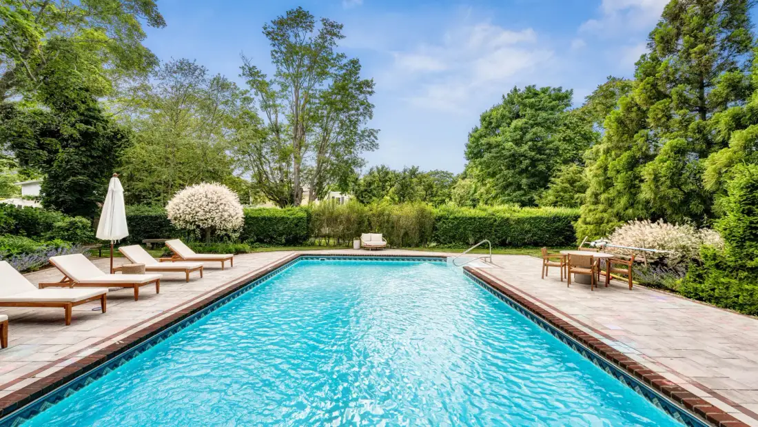 Una piscina rectangular está en un jardín ajardinado con asientos para descansar.