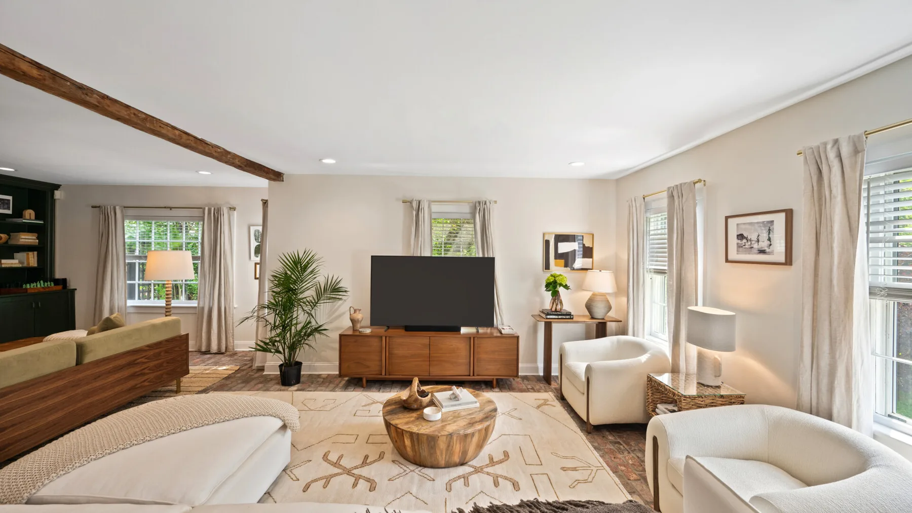 Una sala de estar luminosa con televisor, asientos y ventanales.