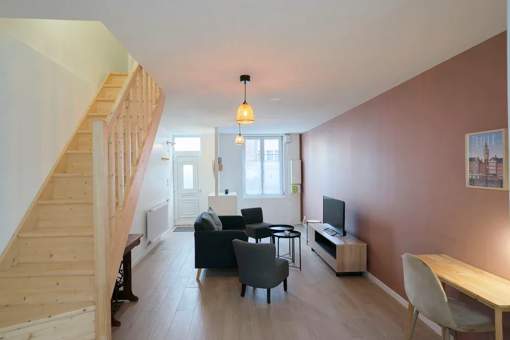 A living and dining area with dark seating, a television, and a staircase.