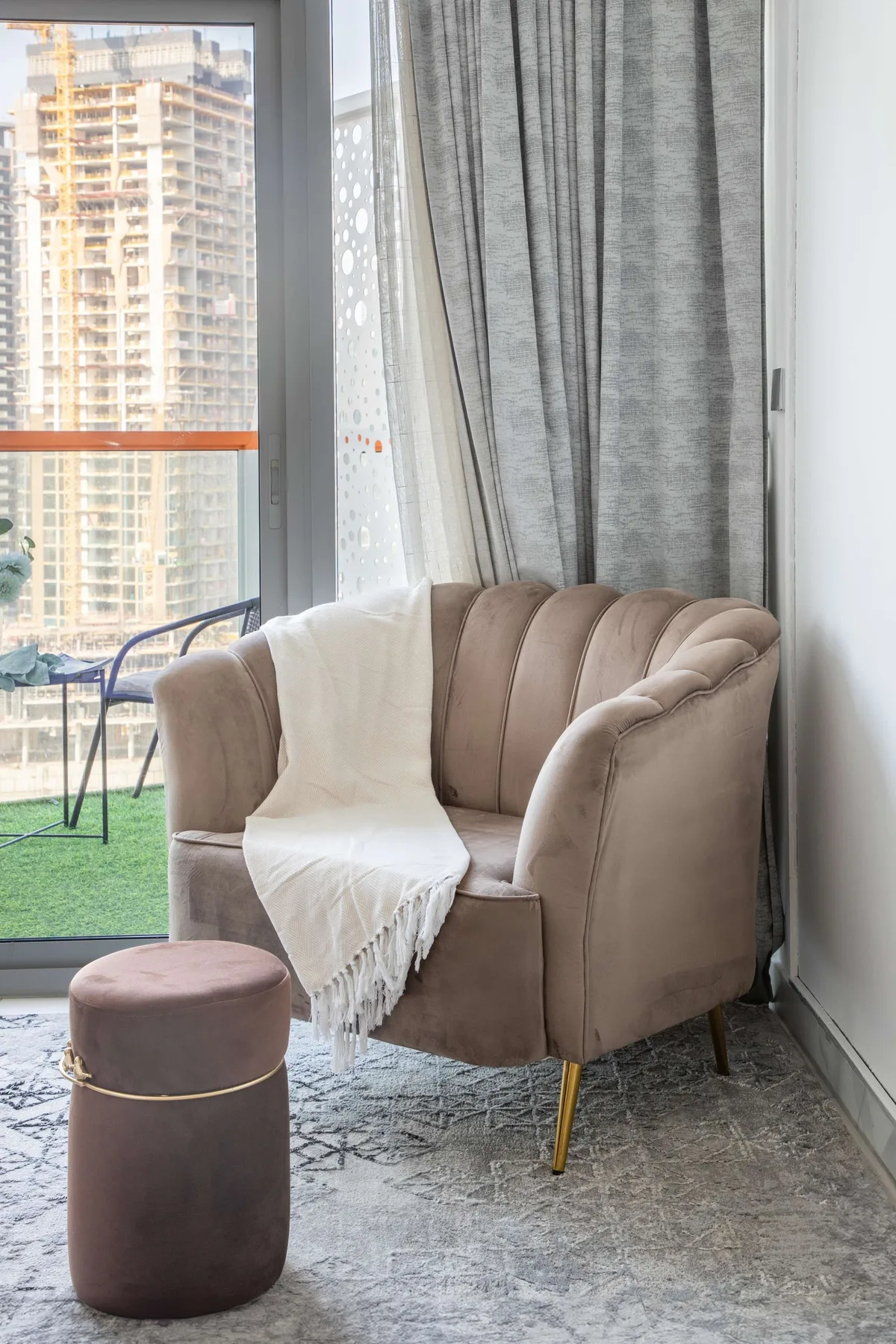 Un sillón acolchado con una manta está junto a una ventana grande.