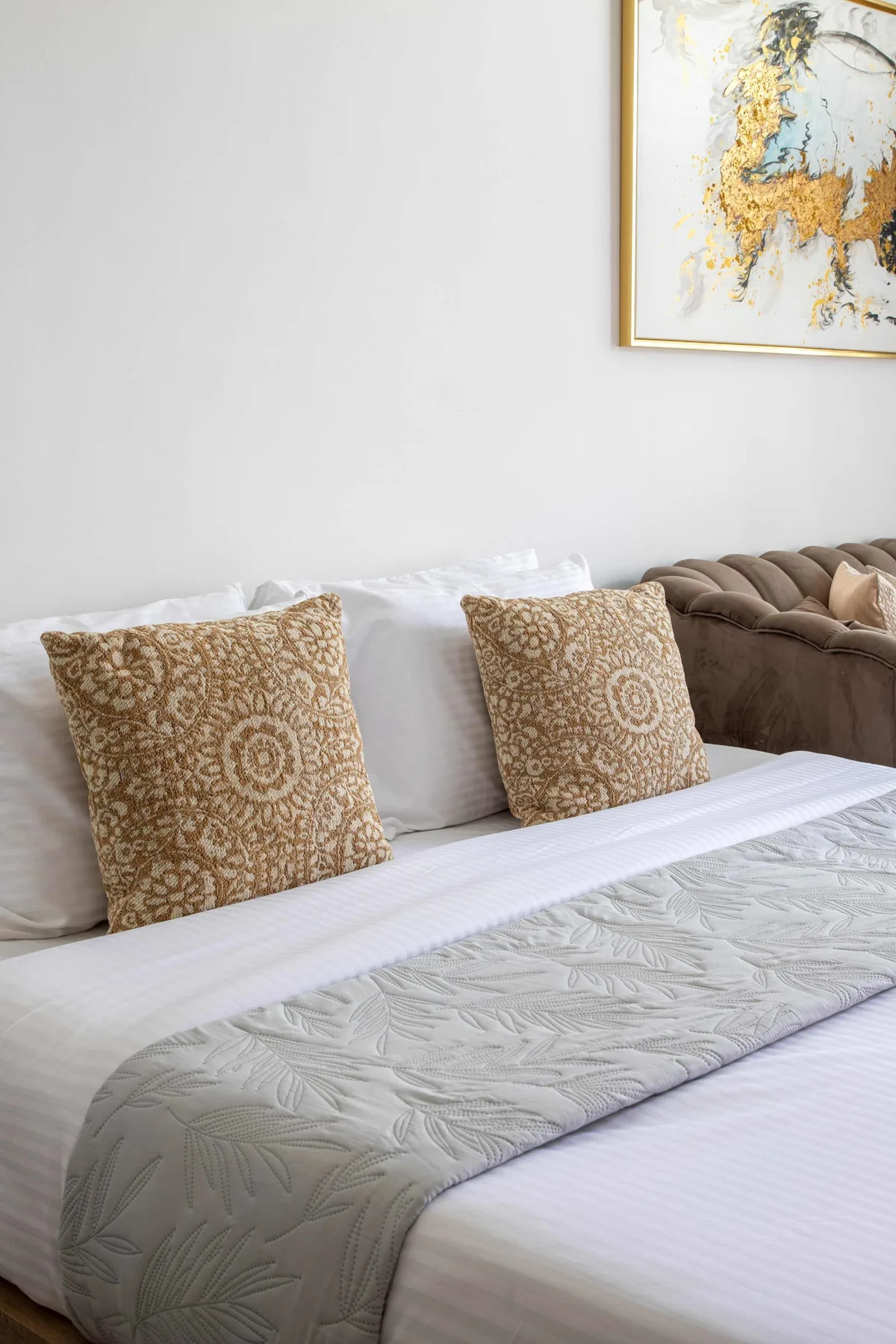 Una cama bien tendida con cojines estampados está junto a una zona de asientos acolchada.