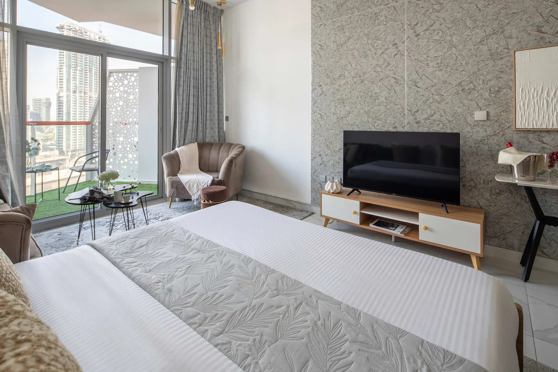 Dormitorio luminoso con una cama grande, un televisor y ventanas de piso a techo.