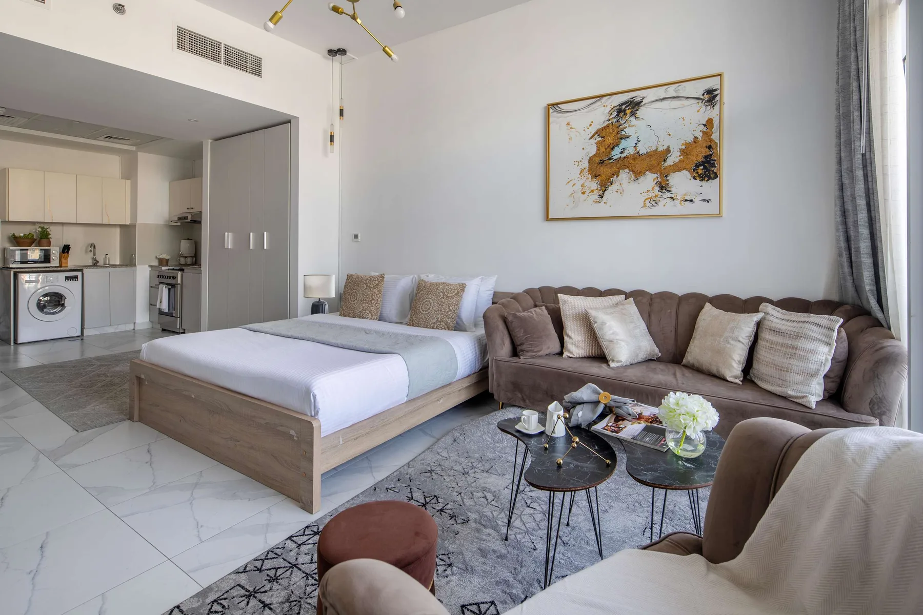 Un estudio con zona de dormitorio y sala de estar, cama, asientos y una pequeña cocina.