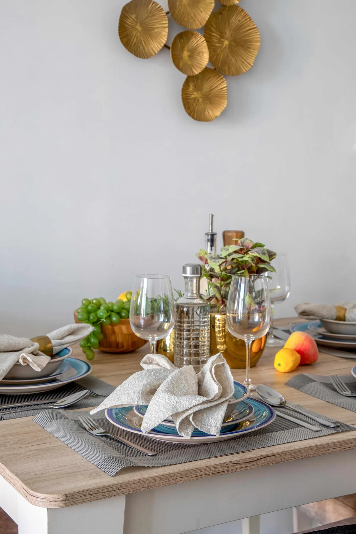 Una mesa está preparada con platos, servilletas dobladas, cristalería y fruta.