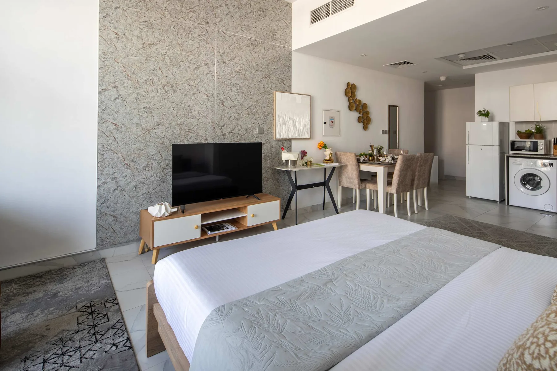 Un dormitorio se abre a un comedor y una cocina compacta, con un televisor junto a la cama.