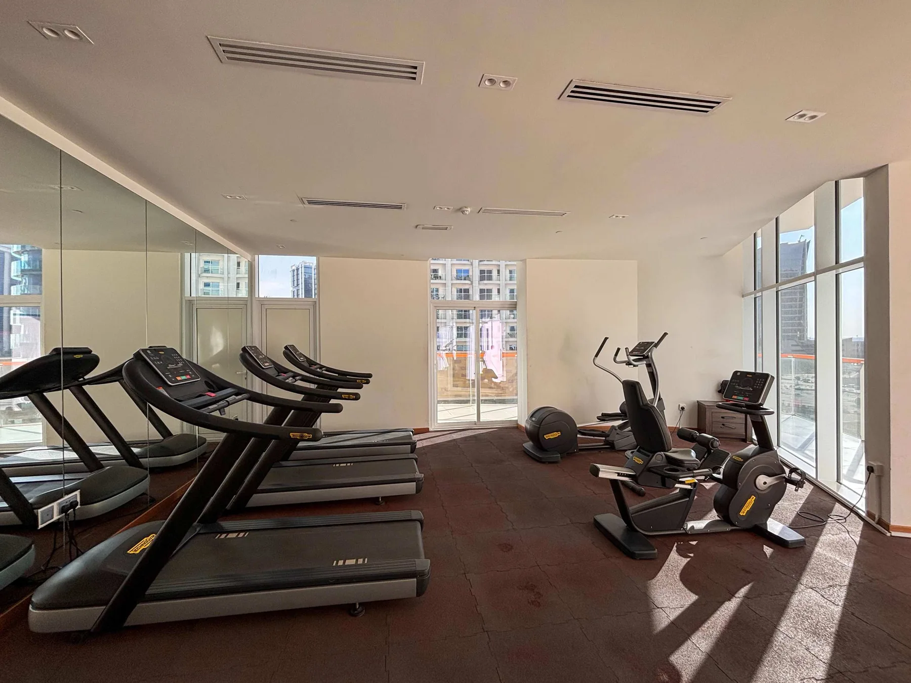 Una sala de ejercicio con cintas de correr a un lado y bicicletas junto a las ventanas.