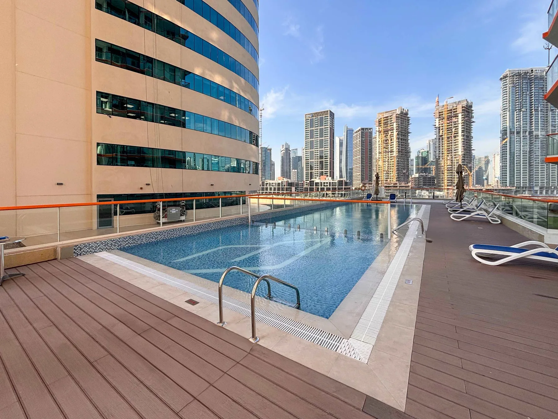 Una piscina en la azotea está junto a una terraza de madera, con edificios de la ciudad al fondo.