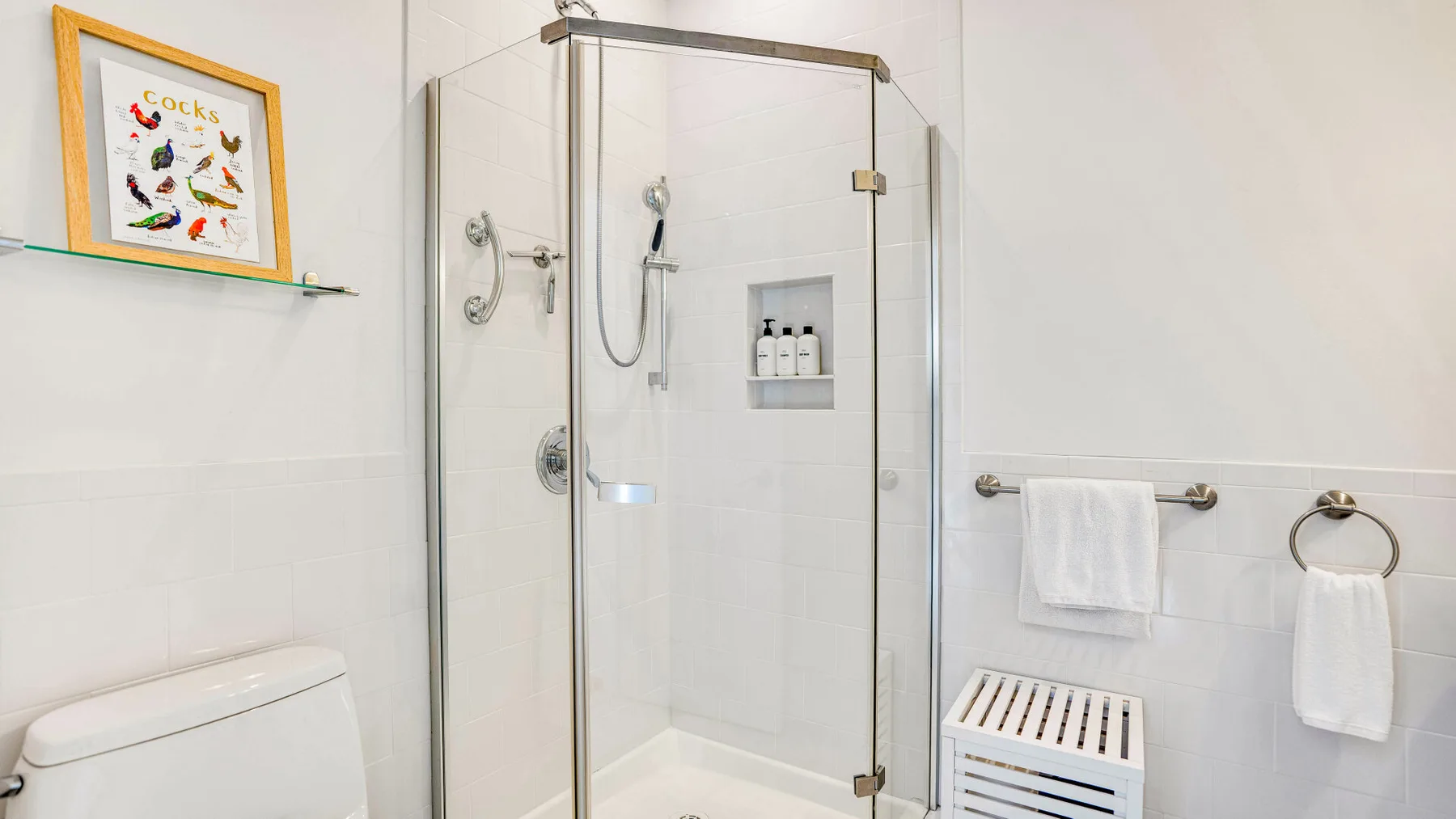 Un baño luminoso con ducha de cristal y azulejos blancos.