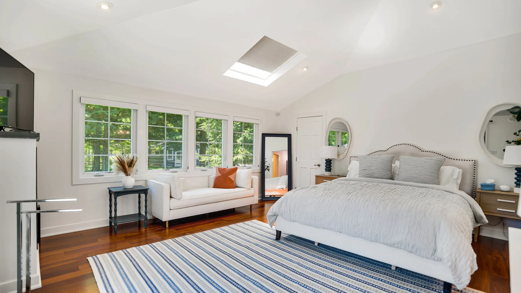 Un dormitorio luminoso con una cama grande, una zona de estar y ventanas amplias.