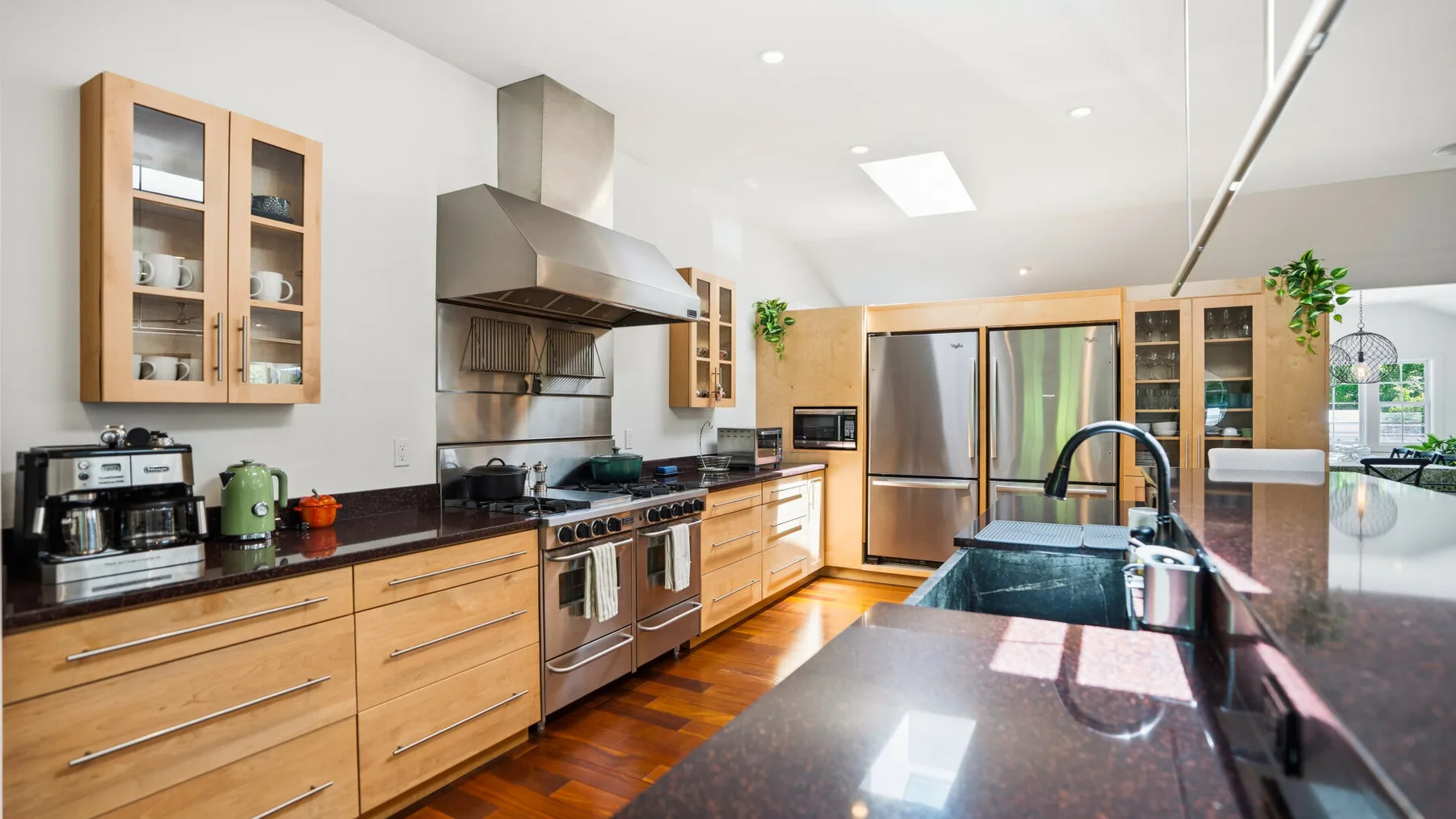 Una cocina luminosa con gabinetes de madera, electrodomésticos de acero inoxidable y una isla oscura.