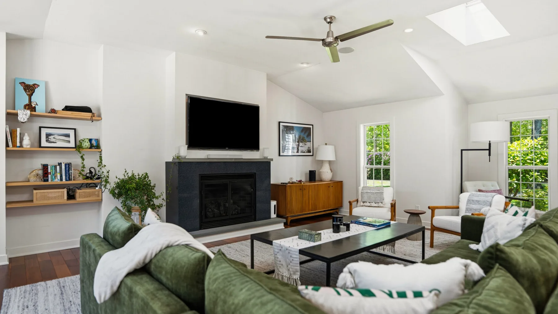 Una sala luminosa con asientos verdes, una chimenea y grandes ventanas.
