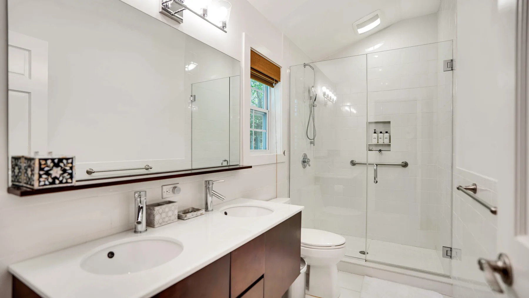 Un baño luminoso con lavabo doble y ducha de vidrio.