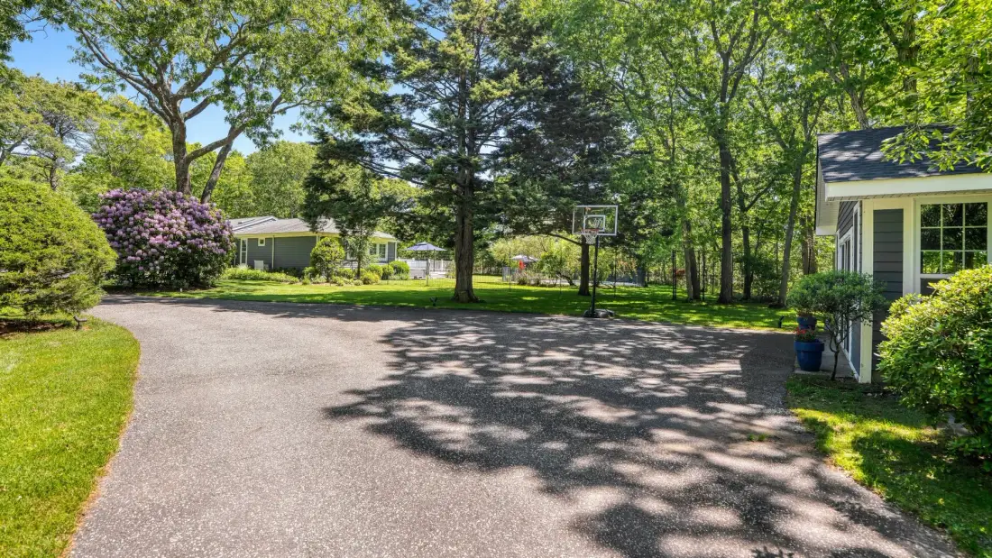 Una entrada arbolada se curva junto a una casa, con una canasta de baloncesto cerca.