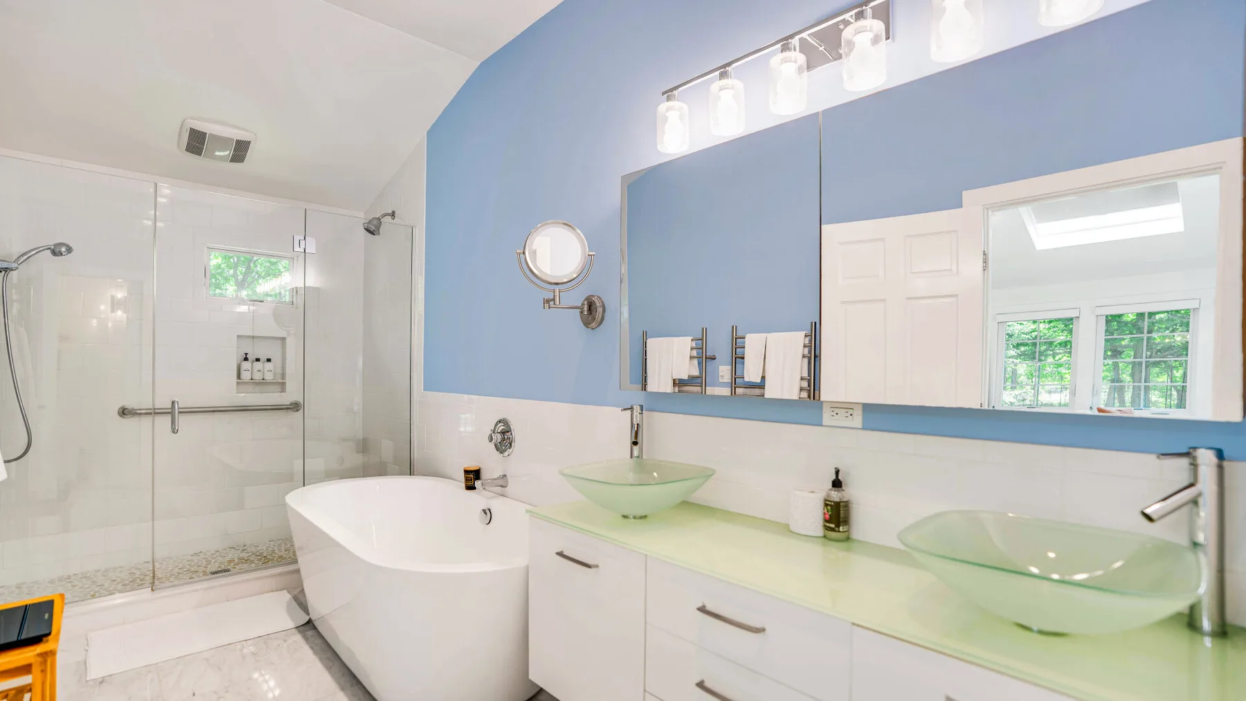 Un baño con una bañera exenta, una ducha de vidrio y dos lavabos verdes sobre encimera.