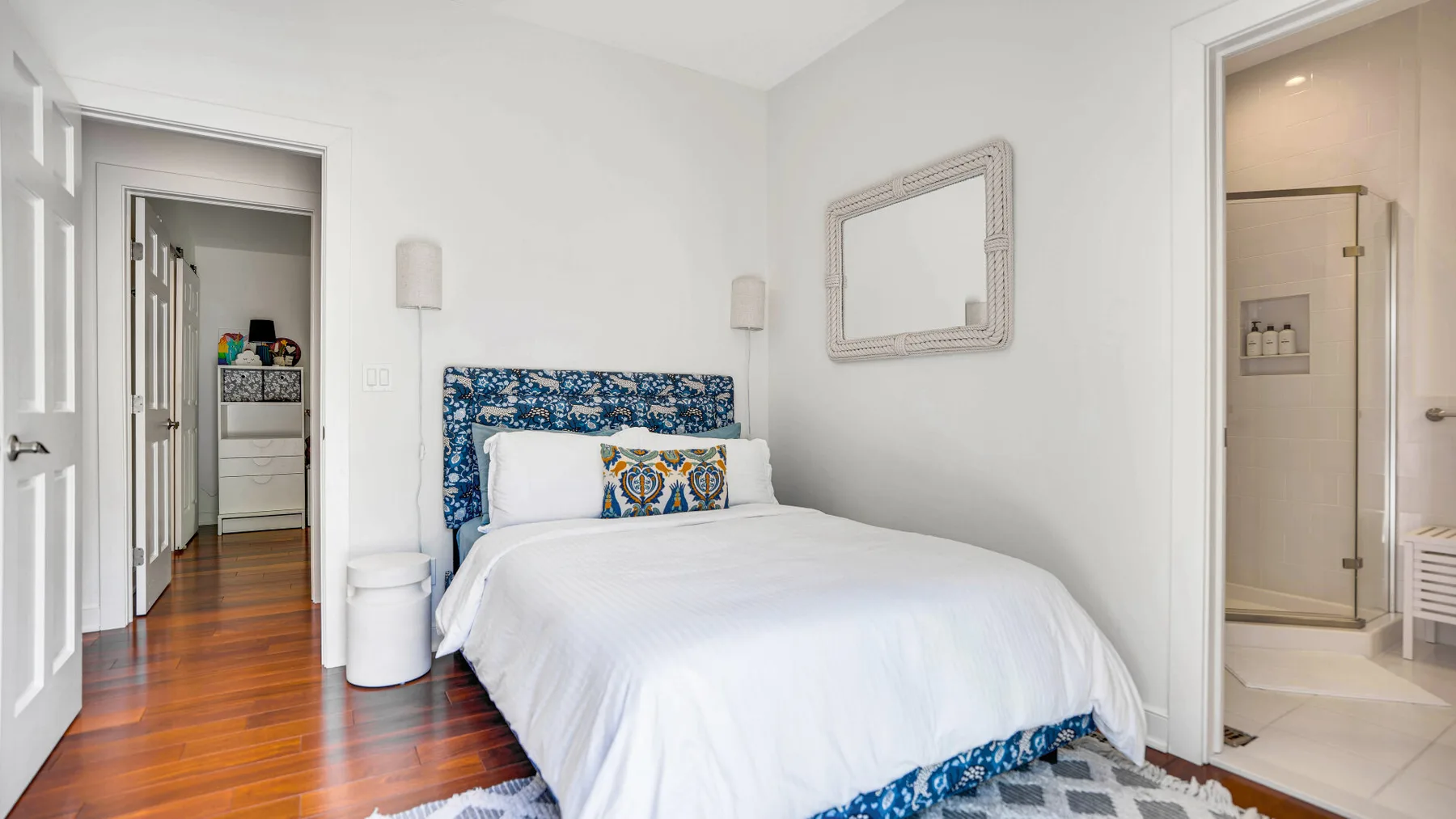 Un dormitorio luminoso con una cama vestida de blanco y ropa de cama estampada en azul.